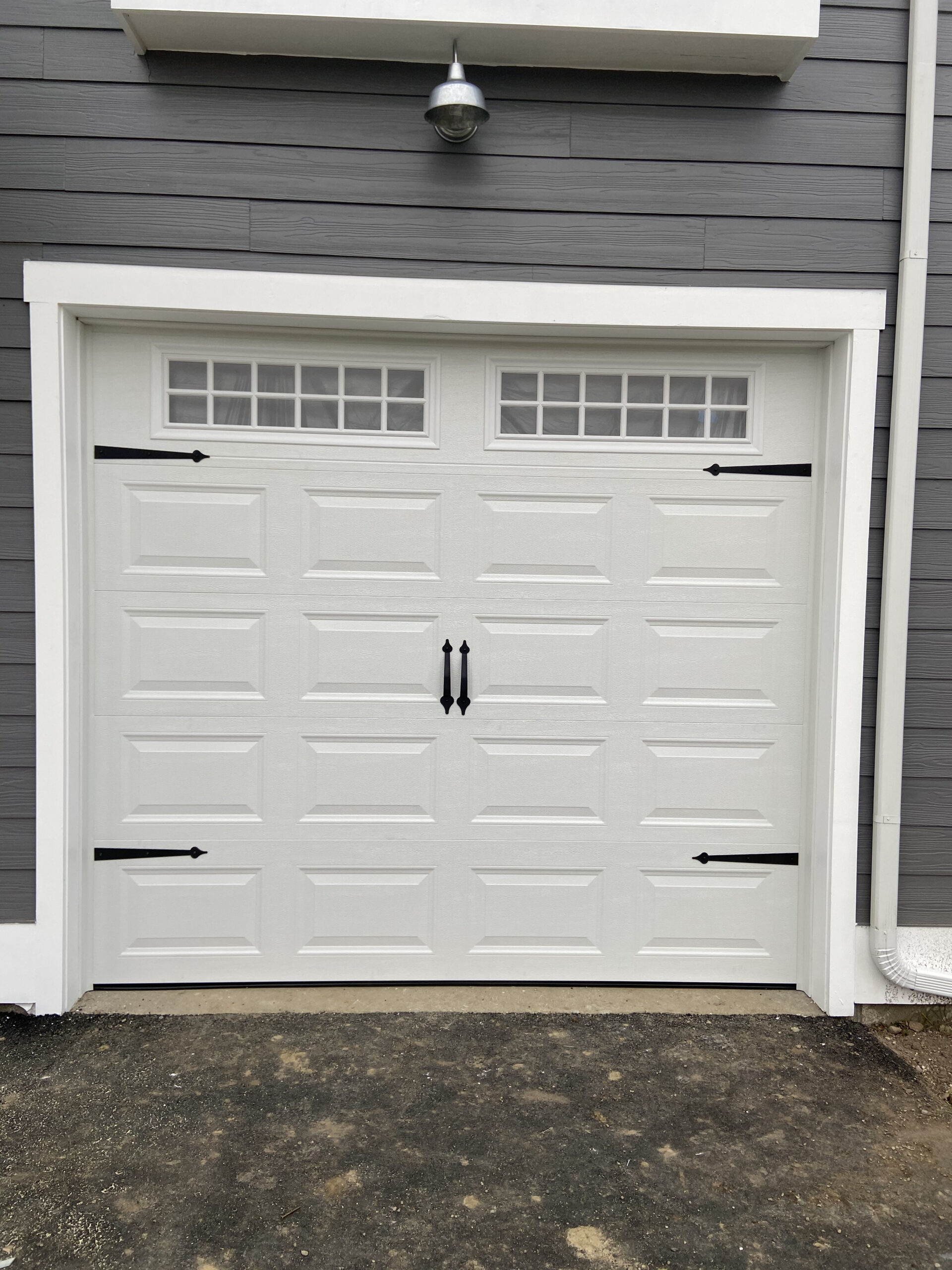 White garage door with black spade-shape handles and hinges and square windows, 