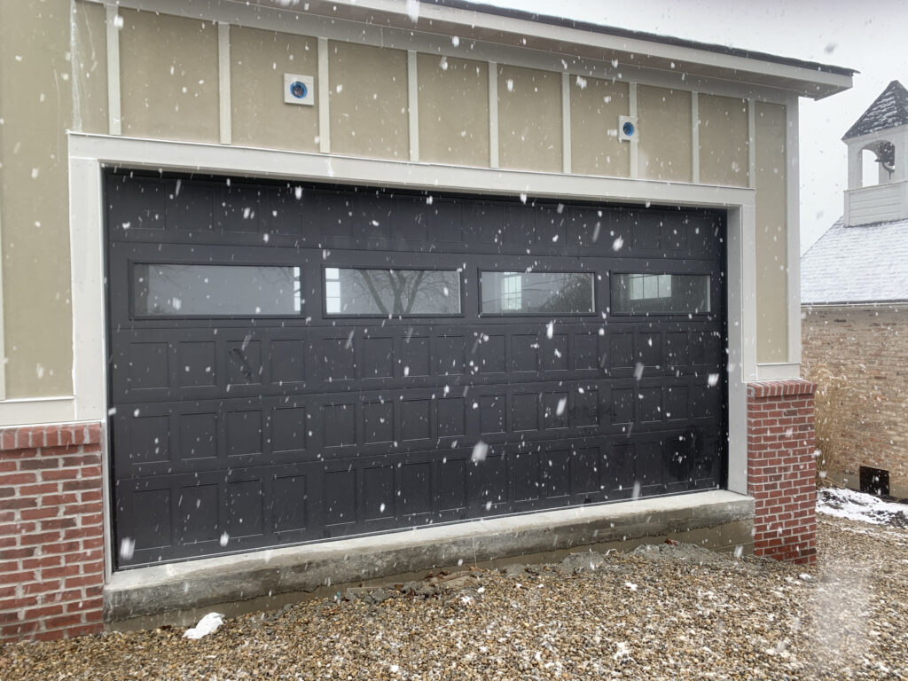 Black modern garage door with windows in the snow